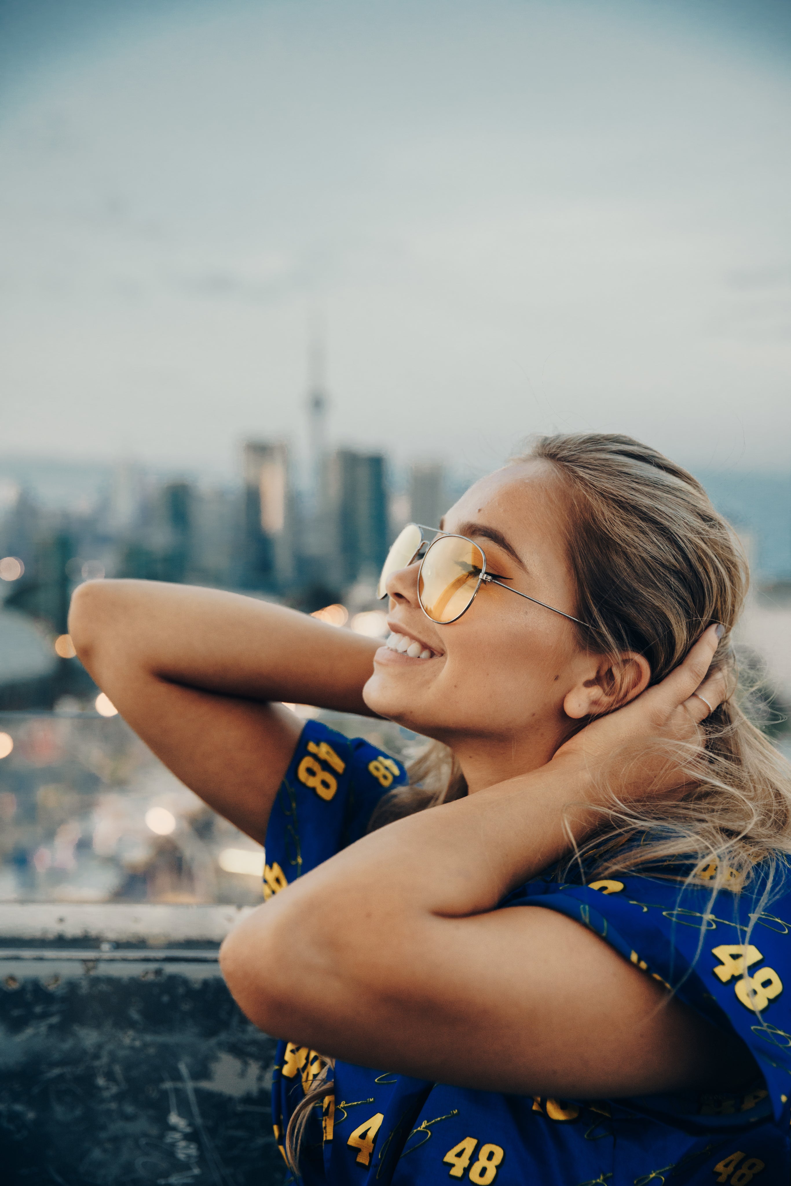 Smiling woman wearing Strange Strains 420 apparel overlooking a city skyline, representing luxury streetwear, wearable art, self-expression, and cannabis-inspired fashion.